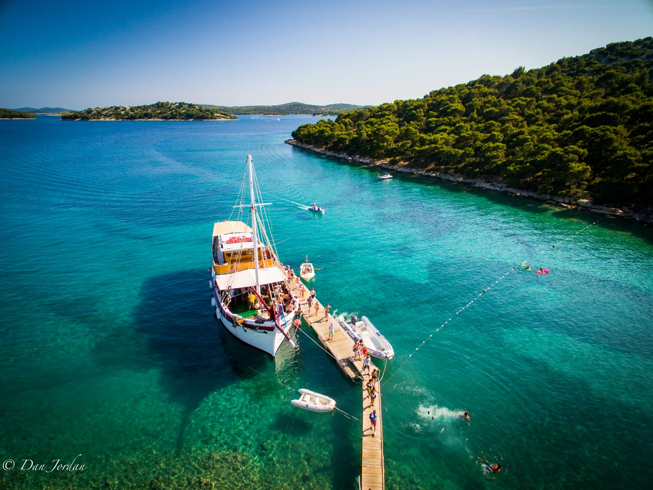 Festival boat beside The Garden Resort jetty, with clear turquoise sea and a wooded coast, in 2016